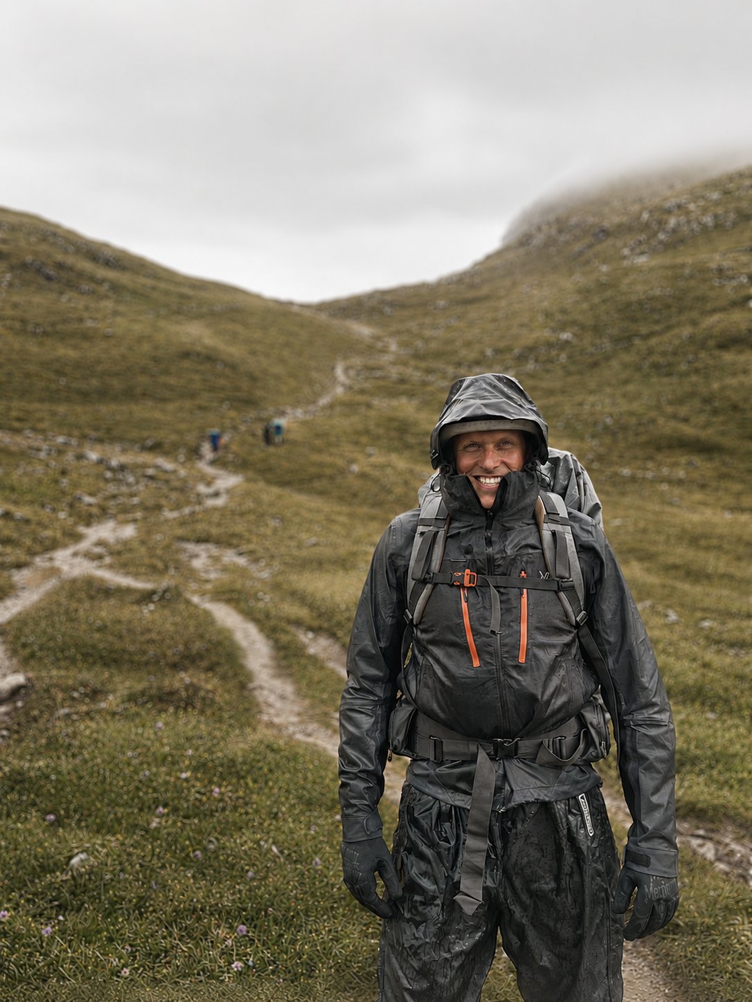David Klapheck beim Wandern in den Alpen, lachend mit wetterfester Ausrüstung